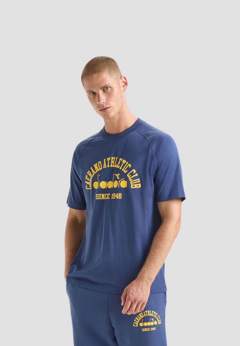 Maglietta sportiva blu navy con testo giallo che recita "Caerano Athletic Club" e logo. Presenta un collo rotondo e maniche corte a raglan.