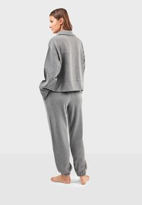 Šedý set pohodlného oblečení se skládá z krátké, boxovité mikiny s límečkem a sladěných zúžených kalhot s elastickými manžetami, vyrobených z měkké látky.