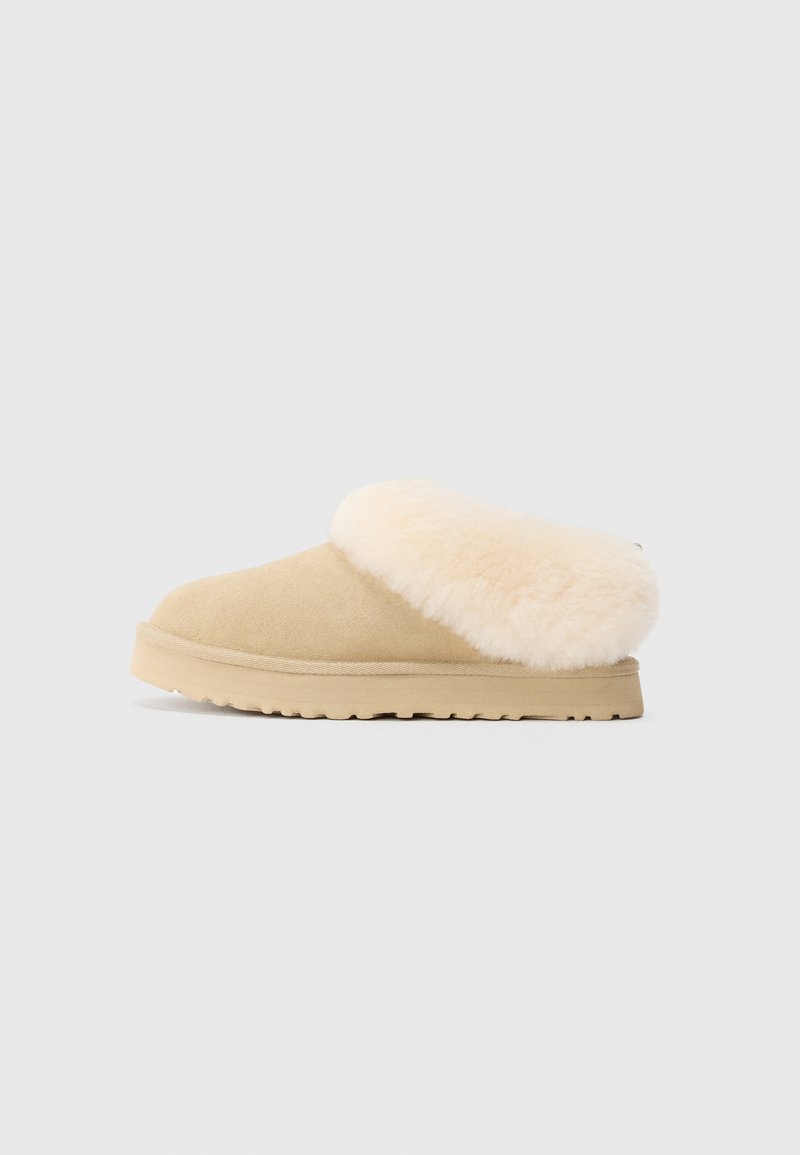 Chausson en suède beige à enfiler avec un épais revers en fourrure synthétique crème douce et une semelle en caoutchouc robuste et texturée.