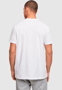 Bílý bavlněný tričko s kulatým výstřihem a krátkými rukávy. Hladká textury, volný střih a jednoduchý design. Zadní pohled nezobrazuje žádné ozdoby.