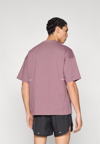 Μπλούζα με κοντά μανίκια σε μωβ απόχρωση, άνετη γραμμή με πλαινές σχισμές, με κείμενο στην πλάτη. Συνδυάζεται με μαύρο σορτς, υφή υφάσματος λεία.