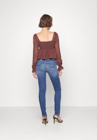 Top de peplum marrón con mangas largas, combinado con jeans ajustados de color azul y sandalias de tacón alto negras. Vista trasera mostrada.