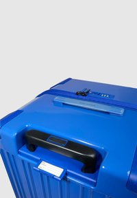 Blauer Hartschalenkoffer mit strukturierter Oberfläche, schwarzem Griff, Reißverschluss und Anhängerhalter. Verfügt über seitlichen Griff und Zahlenkombinationsschloss.