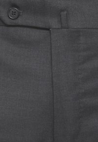 Primo piano di pantaloni in tessuto grigio scuro con una vita visibile, passante per la cintura e un bottone nero con l'etichetta "SLOWEAR".