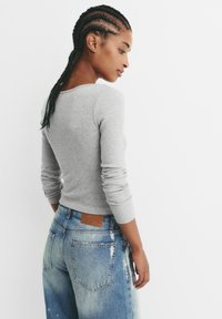 Grijze lange mouwen ribbelshirt gecombineerd met vervaagde blauwe hoge taille jeans. Het shirt heeft een eenvoudige ronde halslijn en aansluitende mouwen.