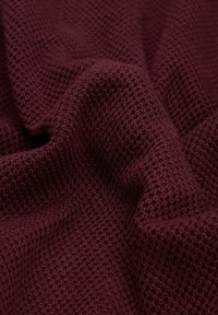 Miękka, teksturowana burgundowa tkanina o wzorze w wafelkowe sploty, pokazana w delikatnych fałdach podkreślających jej grubość i ciepło.