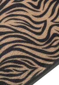 Tappeto beige con motivo a strisce di tigre nere, caratterizzato da una superficie morbida e texturizzata e un bordo, che mette in risalto il suo design audace e il contrasto di colori.