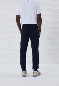 Marineblauwe joggingsbroek met elastische tailleband, zijzak en taps toelopende pijpen, gecombineerd met een wit t-shirt en zilverkleurige sportschoenen.