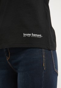 Sort bomulds T-shirt med lige snit, der har hvidt logo tekst nær kanten. Sammen med blå denim jeans, der har et enkelt design.