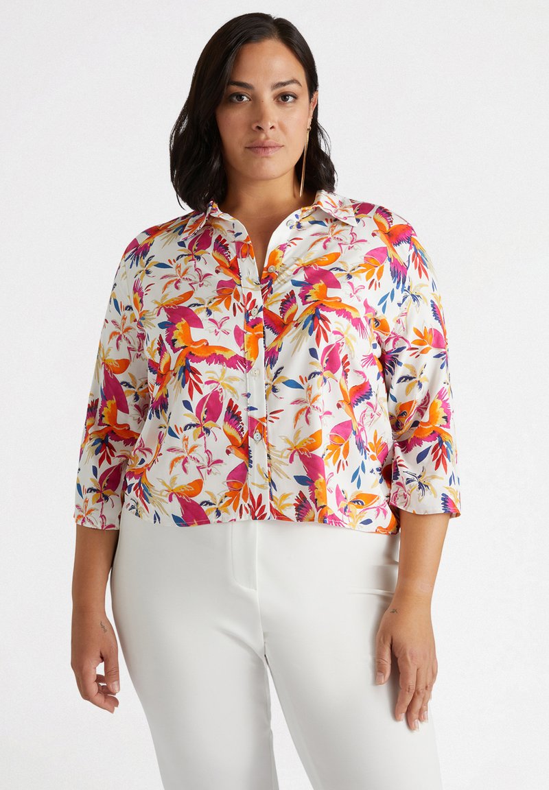 Blusa bianca con un vivace motivo floreale nei colori rosa, arancione e blu. Presenta una chiusura con bottoni e maniche a tre quarti.