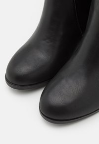 Une paire de bottes en cuir noir lisse à bouts ronds sur un fond blanc.