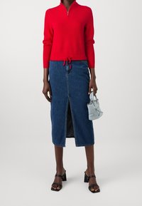 Pull rouge côtelé avec un col zippé, associé à une jupe midi en denim avec une fente à l'avant. Les accessoires comprennent un sac à main bleu clair et des talons carrés noirs.