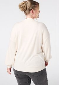 Crème kleurige trui met een losse pasvorm en afhangende schouders. Zachte textuur en geribde zoom. Gecombineerd met donkergrijze strakke broek.