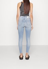 Jeans skinny de color azul claro con una cintura alta y dos bolsillos traseros, combinados con una blusa sin mangas a rayas blancas y negras.
