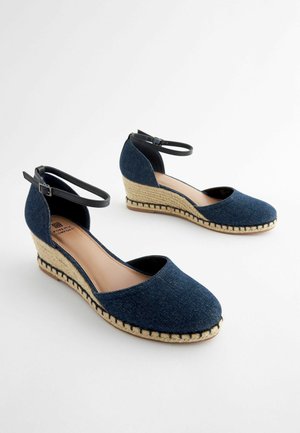 Denimi kallekavatsed mustade pahklipruttidega, looduslikest jute detailidega ja ümarate varvaste disainiga. Tekstureeritud kangas kontrastsete õmblustega.