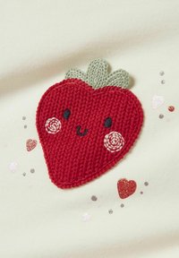 Punainen broderad mansikka vihreillä lehdillä, hymyilevä naama, ympäröity pienillä värikkäillä kimaltelevilla sydämillä ja pisteillä vaalealla kankaan taustalla.