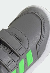 Szary syntetyczny sneaker z teksturowaną powierzchnią, z dwoma zielonymi pionowymi paskami, paskami na rzep i białą gumową podeszwą.