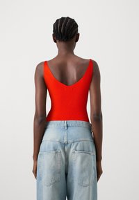 Geribbelde rode bodysuit met een diepe V-rug, gecombineerd met lichtblauwe hoogsluitende jeans met twee achterzakken en een rechte pijp.