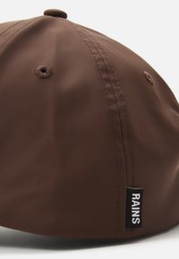 Casquette imperméable marron avec une couronne arrondie, des coutures subtiles et une étiquette sur le côté portant le texte "RAINS". Texture lisse et finition mate.