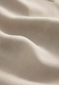 Cream-colored fabric with a smooth, slightly shiny texture, showing soft, flowing folds and a subtle sheen.