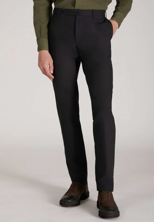 Zwarte op maat gemaakte broek met een gladde afwerking, slim fit ontwerp, riemlussen en een één-knops sluiting. Gecombineerd met bruine schoenen.