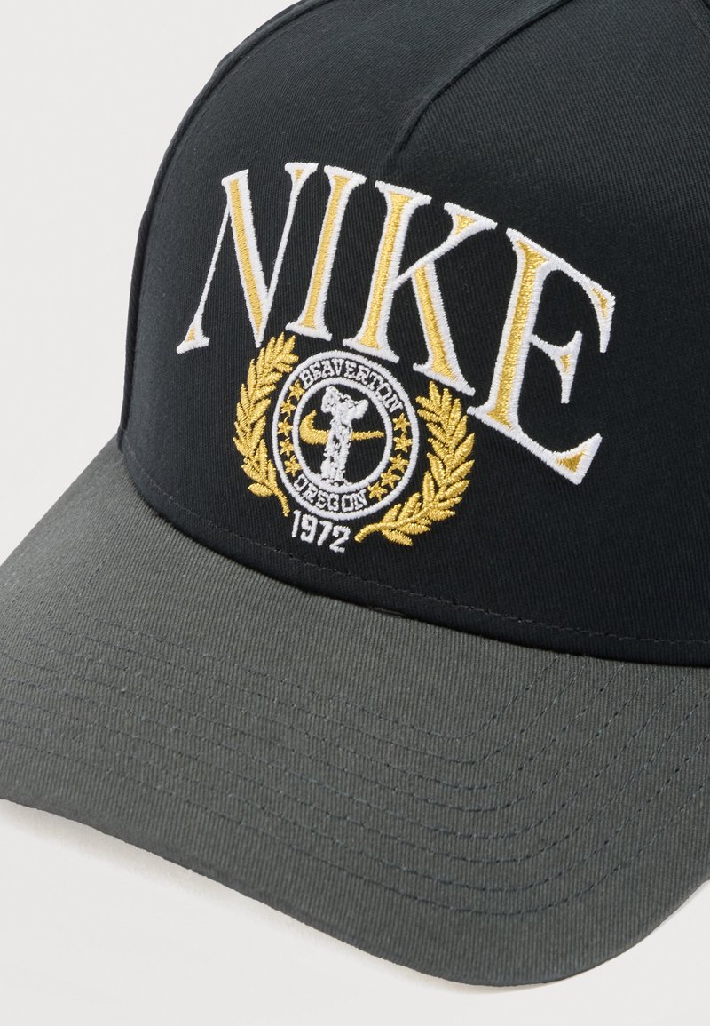 Black and gray cap with yellow and white embroidered "NIKE," "Beaverton Oregon," and "1972" beneath a circular design with a laurel wreath.