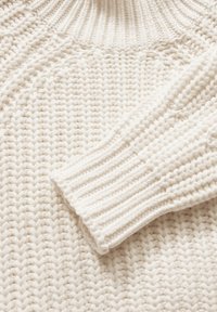 Cremfarbener Strickpullover mit einem groben, gerippten Kragen und einem strukturierten, Zickzackmuster über den Körper und die Ärmel.