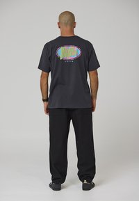 Dunkelgraues T-Shirt mit buntem "Riviera Projects"-Grafik auf der Rückseite, kombiniert mit schwarzer Hose. Einfaches Design, Baumwollmaterial.