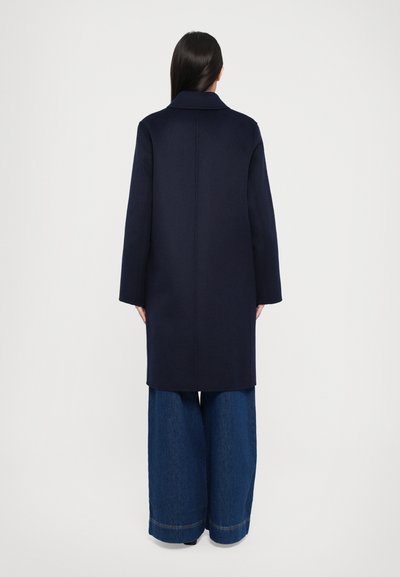 Marineblauwe wollen jas met een rechte silhouet, wijde mouwen en een notch-revers, gecombineerd met brede denim broeken.