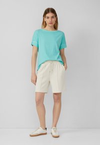 Lichtblauwe t-shirt met opgerolde mouwen, gecombineerd met beige shorts met een trekkoord in de taille, en witte sneakers met een tan zool.