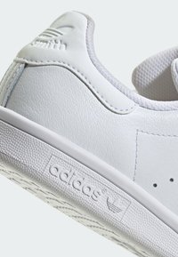 Λευκό δερμάτινο sneaker με υφή, με μινιμαλιστικό σχέδιο, λογότυπα και ομαλή καουτσούκ σόλα. Κλασικό στυλ τένις.