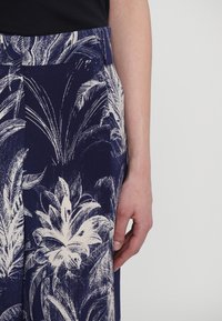 Navy trousers featuring a white tropical leaf print, made from lightweight fabric, with a flat waistband and side pockets.