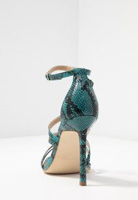 Teal ja must gasto ka snakeskin kõrge kontsaga sandaalid, millel on õhuke pahkluu rihm ja stiletto konts. Sile tekstuur läikiva viimistlusega.
