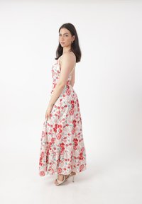 Blumenkleid im Maxistil mit weißem Hintergrund, das rote und pinke Rosen zeigt. Es hat dünne Spaghettiträger und einen flatternden, Rüschensaum.