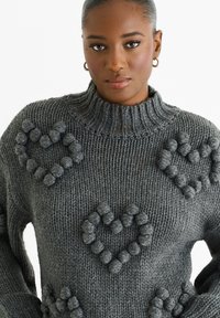 Maglione a collo alto di colore grigio scuro, lavorato a maglia, con dettagli testurizzati a forma di cuore. Realizzato in filato spesso, presenta una vestibilità comoda.