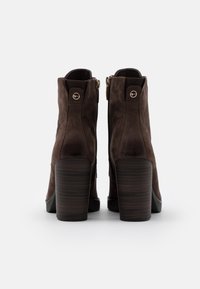 Braune Wildleder-Stiefeletten mit hohem Blockabsatz, seitlichen Reißverschlüssen und kreisförmigen Akzenten am Knöchel. Glatte Textur mit schlanker Silhouette.