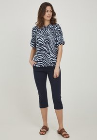 Navy och ljusblå zebra-mönstrad topp med korta ärmar, i kombination med marinblå capribyxor. Bruna sandaler med två remmar fulländar looken.