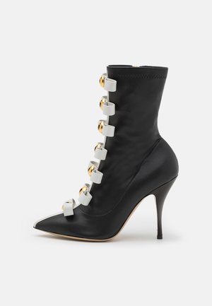 Czarne wysokie botki na obcasie z wydłużonym noskiem, z białymi paskami i złotymi akcentami po bokach, wykonane z gładkiej skóry.