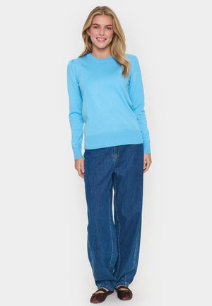 Lichtblauwe gebreide sweater met lange mouwen en ribbels aan de onderkant, gecombineerd met blauwe wijde jeans en bruine ballerina's. Geen patronen of opvallende accenten.