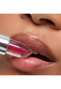Clear lip gloss with a pink tint being applied to full, shiny lips. Lips have a smooth texture and subtle natural color, highlighting the gloss.