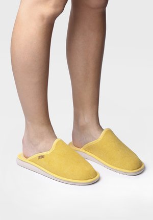 Scarpe slip-on gialle con un upper in tessuto morbido, punta rotonda e suola in gomma bianca. Dettaglio delle cuciture e etichetta del marchio visibile.