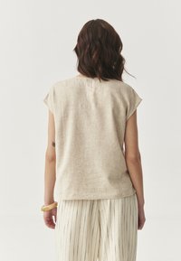 Top in lino beige con una vestibilità rilassata, maniche a cappuccio e orlo dritto. Abbinato a pantaloni a gamba larga a strisce di colore chiaro.