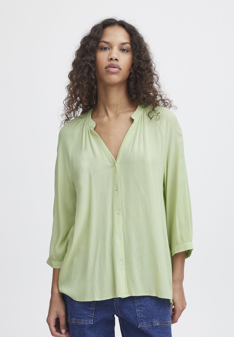 Camicia button-up verde chiaro con maniche lunghe, texture morbida, dettagli con patta e vestibilità rilassata.