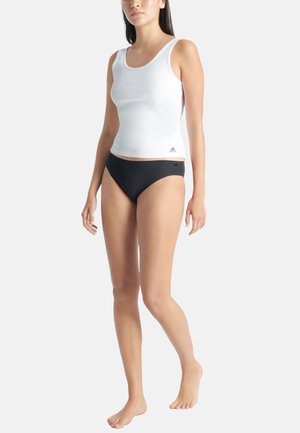 Top bianco senza maniche con texture a coste e spalline larghe, abbinato a slip bikini neri. Dettaglio del logo in basso a sinistra del top.