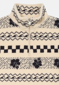 Pullover in pile con zip a un quarto di tonalità crema chiaro, caratterizzato da motivi geometrici neri, design floreali e onde, con dettagli in metallo sulla zip.