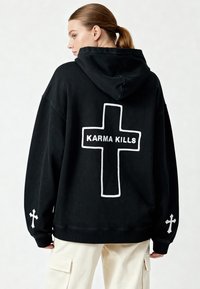 Felpa nera con cappuccio, dalla vestibilità oversize, con una grande croce contornata di bianco e il testo "KARMA KILLS" sulla schiena, oltre a croci bianche sulle maniche.