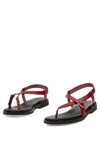 Sandalias rojas con tiras, suela plana y un diseño simple de hebilla, con tiras cruzadas y un estilo clásico de dedo en el pie tipo chancla.