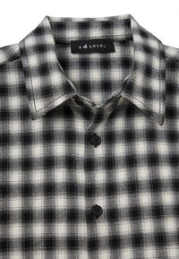 Chemise à carreaux noir et blanc avec un col, comportant deux boutons noirs et un tissu texturé avec des motifs en grille.