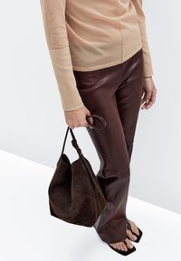 Brune læder flared bukser parret med en lys beige langærmet top. En mørkebrun suede taske holdes i hånden.
