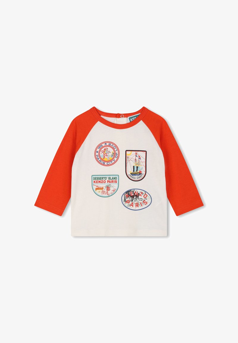 Chemise blanche à manches longues avec manches raglan rouges. Comprend plusieurs patchs colorés avec divers motifs et textes, dont "Kenzo Paris".